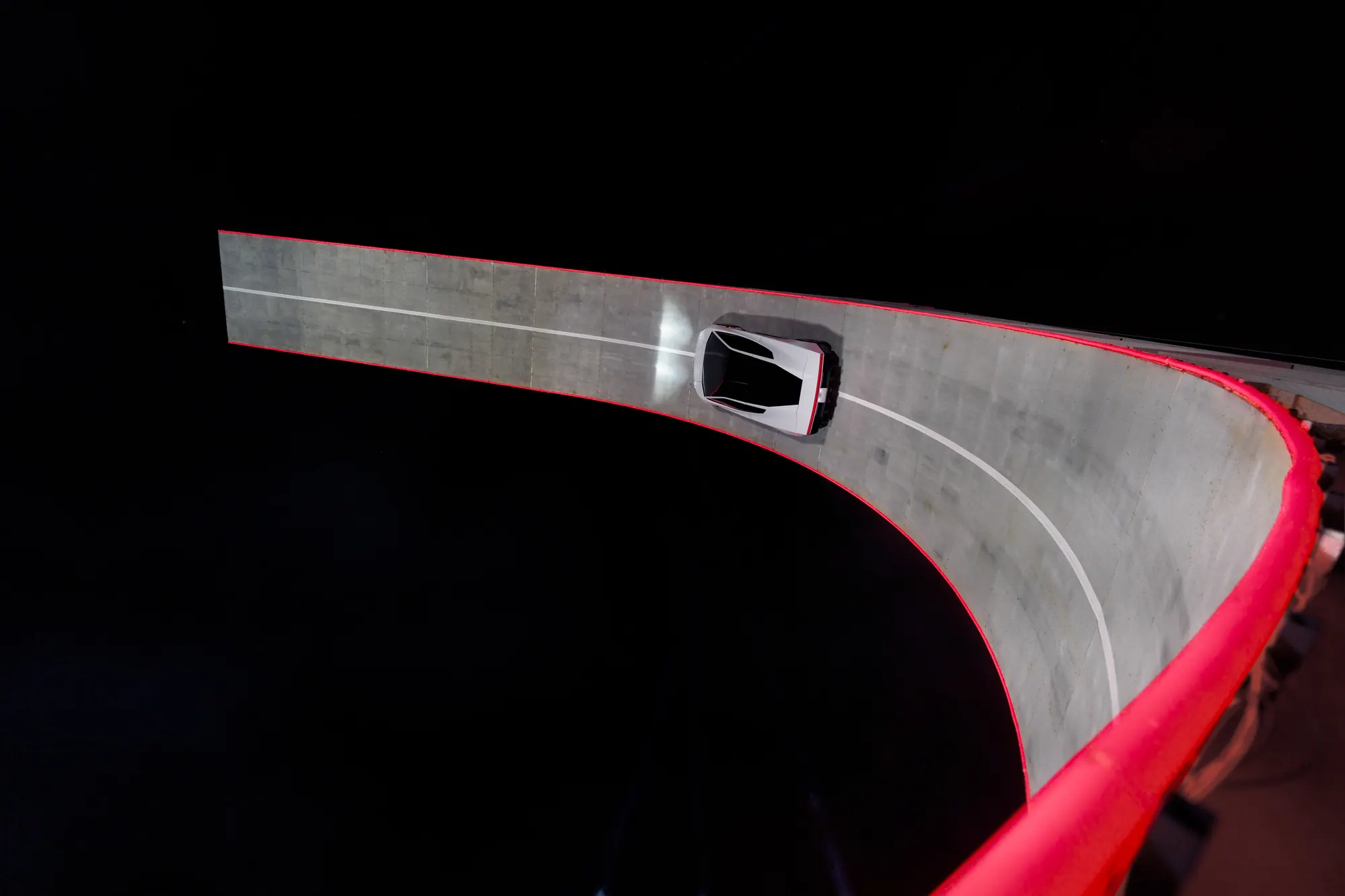 Overhead view of the white Roadster on a curved ramp with a red outer edge and white lane markings.