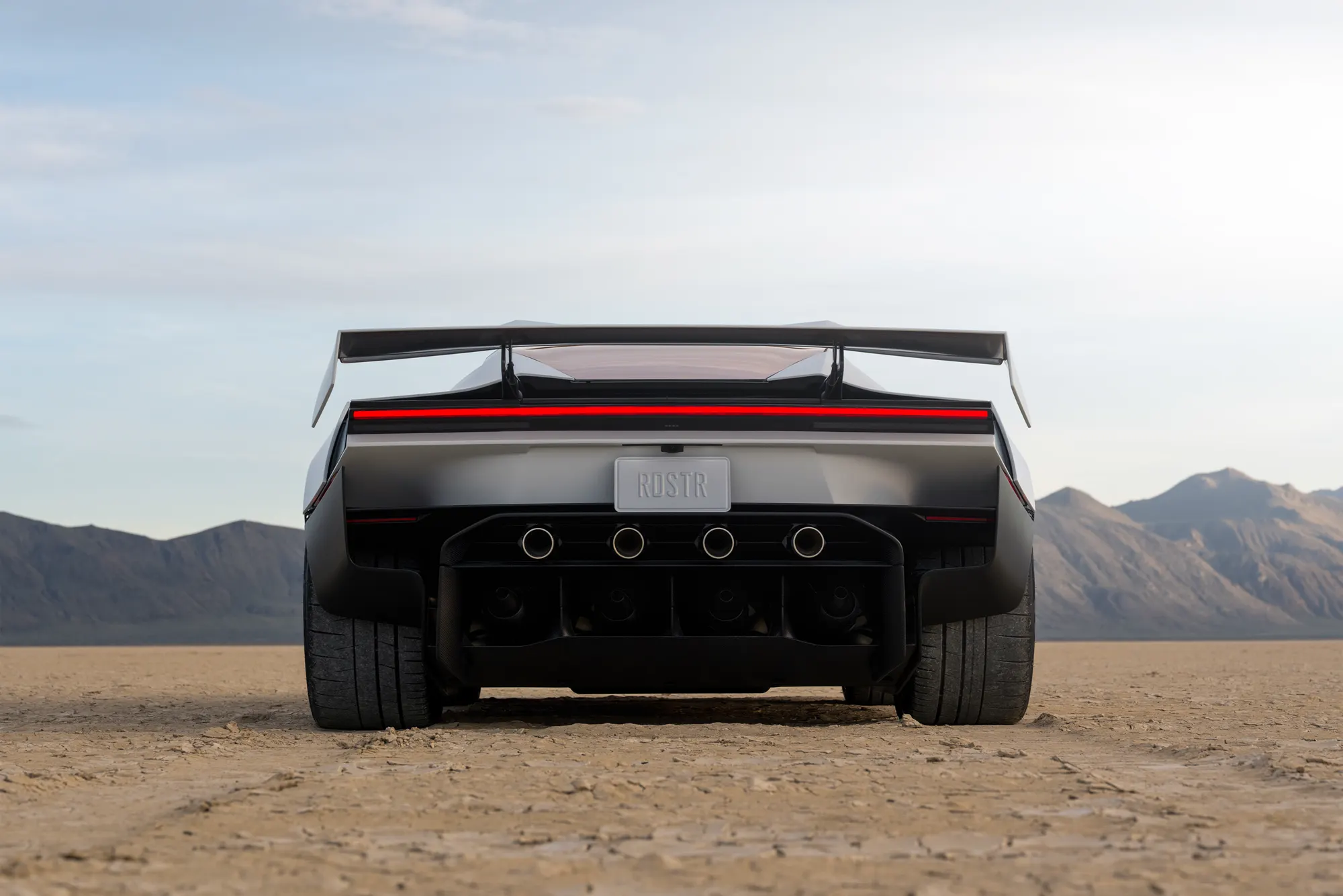 Rear view of the Roadster on the lakebed with the wing raised, showing four round outlets in the diffuser.