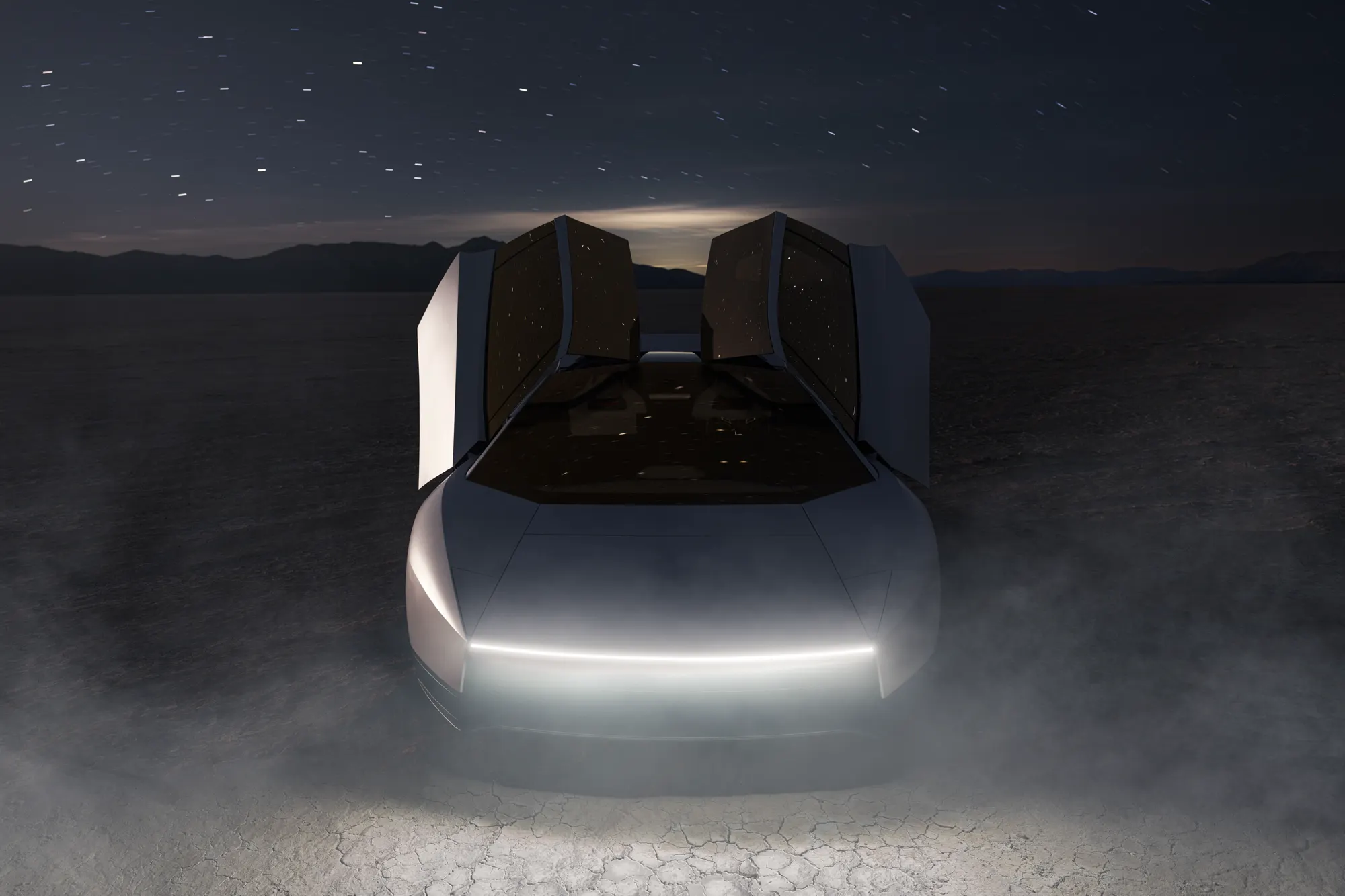 White Roadster at night on a dry lakebed, doors raised, with a light bar across the nose.