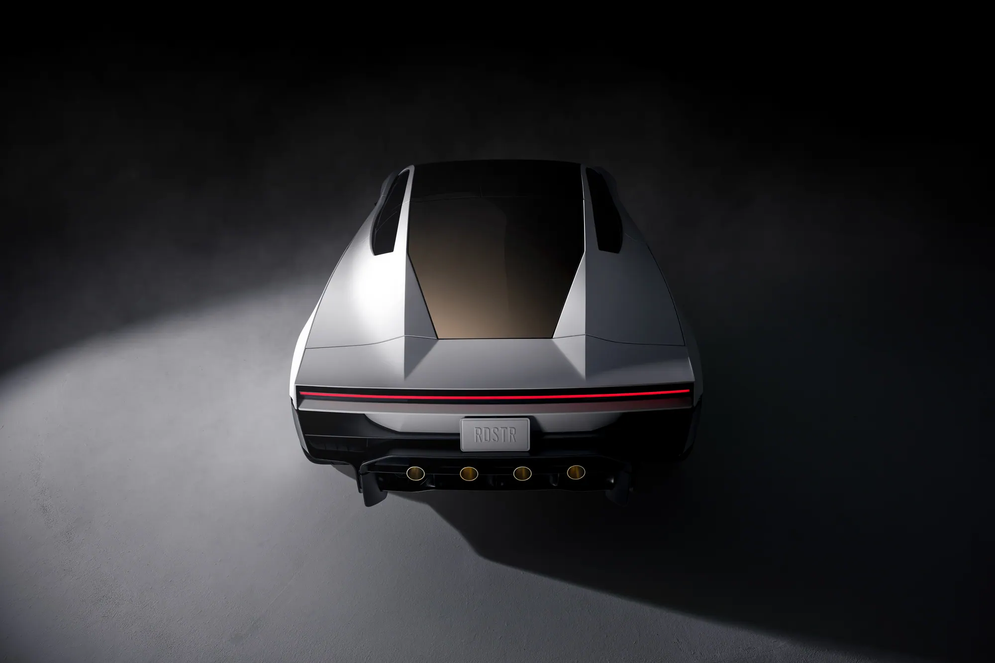 Overhead rear view of the white Roadster, with the wing down, gold-tinted roof glass, a full-width light bar, and four gold-ringed nozzles. The plate reads RDSTR.