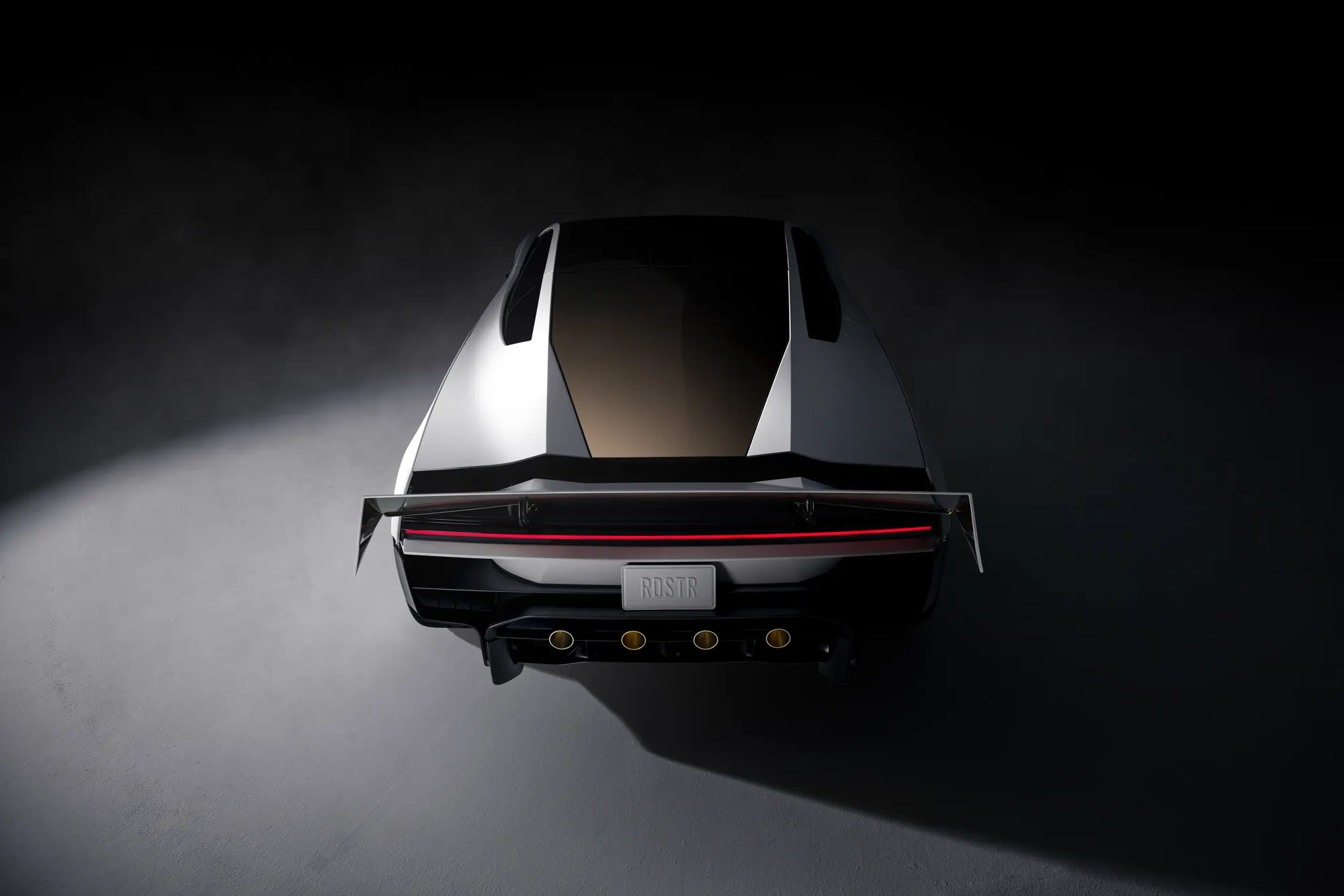 Rear three-quarter studio view of the white Roadster with the rear wing raised and four gold-ringed nozzles above the diffuser. The plate reads RDSTR.