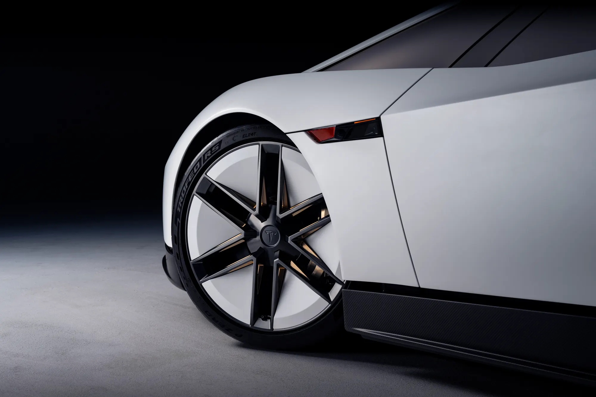 Wheel of the white Roadster, with thin spokes, a Tesla centre cap, and a Pirelli P Zero Trofeo RS tyre.